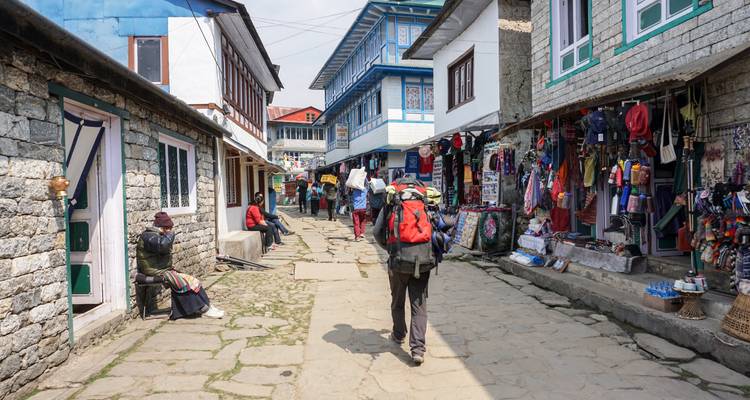 Backpacker walks through stone-paved Himalayan village lined with shops and teahouses