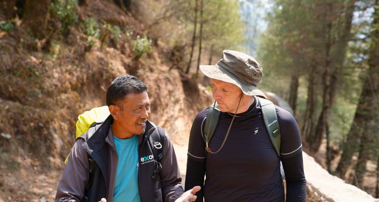 Two trekkers converse on a forest trail in the Nepalese mountains