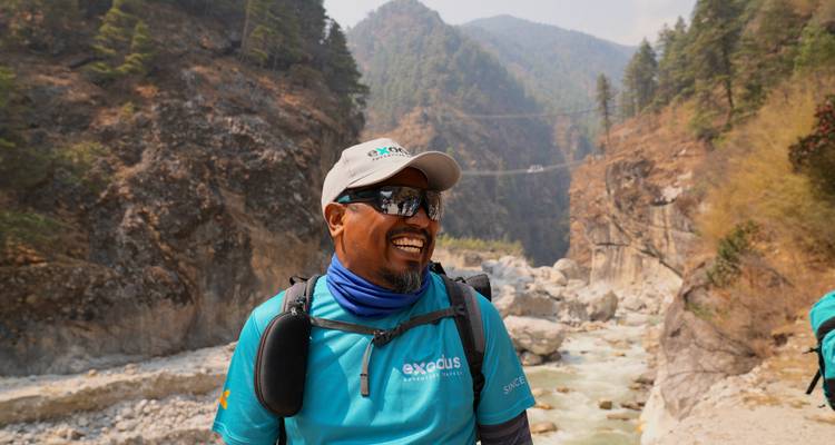 Smiling guide with river gorge and suspension bridge backdrop in the Himalayas
