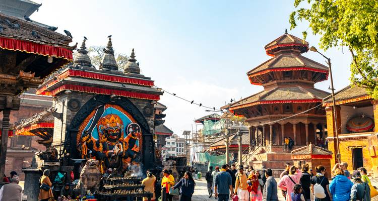 Bustling Kathmandu temple square adorned with vivid deity mural and tiered pagodas