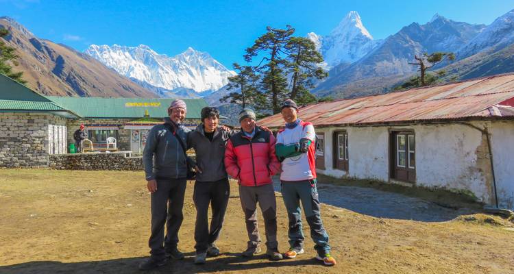 Small trekking team poses with snowy Himalayan giants behind rustic stone buildings