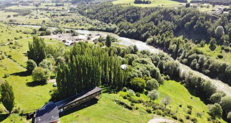 Vista aérea de un río que serpentea a través de un terreno de valle verde con un albergue aislado abajo