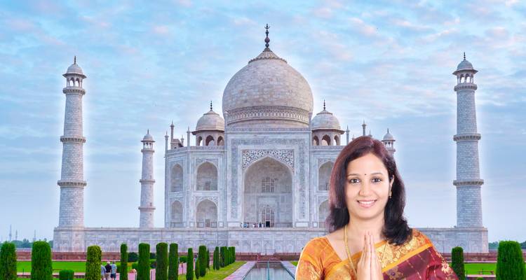 Frau in Sari mit zusammengelegten Handflächen posiert vor dem Taj Mahal an einem bewölkten Morgen.