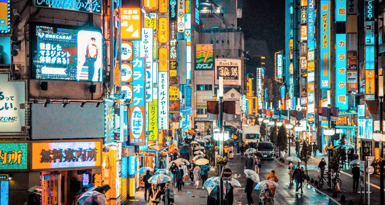 Eine belebte Stadtstraße, die nachts von hellen Neonschildern erleuchtet wird.