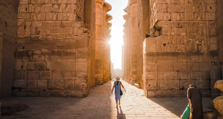 Couloir de temple antique ensoleillé avec un touriste qui marche.