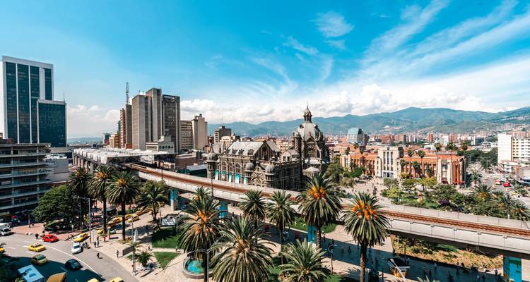 Panoramisch skyline van Medellin met verhoogde metrolijn en palmbomen op de voorgrond