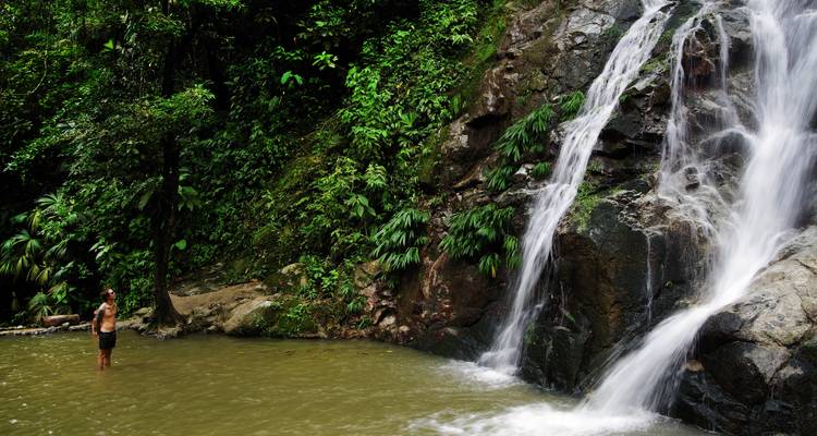 Reiziger die in een ondiep poeltje onder een jungle waterval staat, omringd door groen