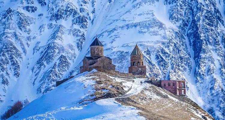 Complejo de iglesia de piedra encaramado en una cresta nevada contra un telón de fondo de empinadas caras montañosas heladas