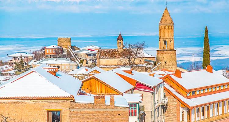 Encantador pueblo en la ladera con casas de techos rojos y torre de iglesia espolvoreada de nieve con vista a un amplio valle