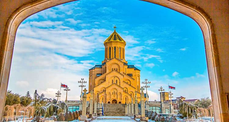 Gran catedral dorada enmarcada por una entrada arqueada bajo un cielo brillante con parches de nieve en el suelo