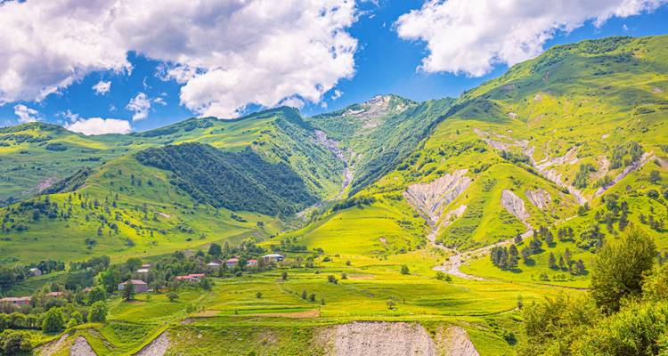 Exuberantes montañas verdes del Cáucaso y valle bajo un cielo azul brillante con nubes dispersas