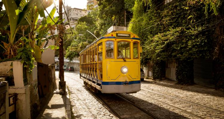 A yellow tram on a cobbled street surrounded by greenery.
