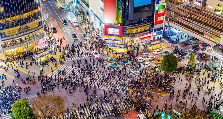 Crowded city intersection with numerous people crossing and buildings surrounding.