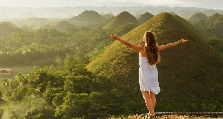 Person steht fröhlich vor den Chocolate Hills.