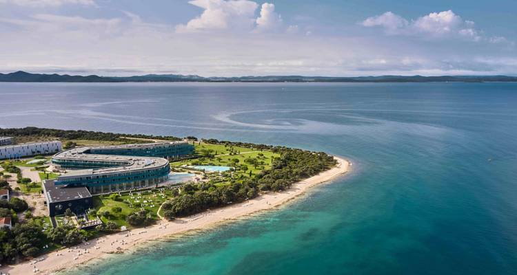 Luchtfoto van een kustlijn met moderne gebouwen, een strand en een blauwe zee.