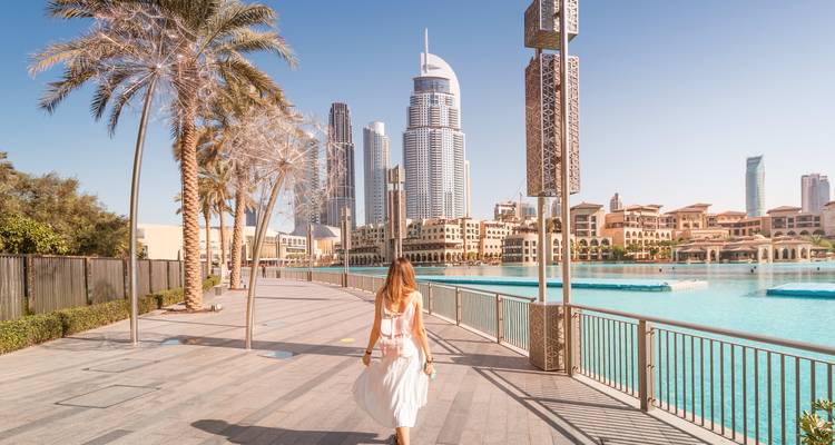 Eine Frau, die auf einer Promenade entlanggeht, mit Dubais Wolkenkratzern im Hintergrund.