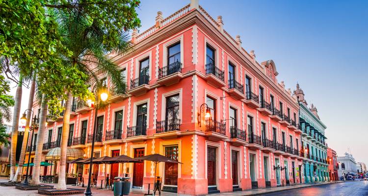 Los vibrantes edificios coloniales con balcones de hierro forjado brillan con una suave luz vespertina en una esquina de una calle de Merida.