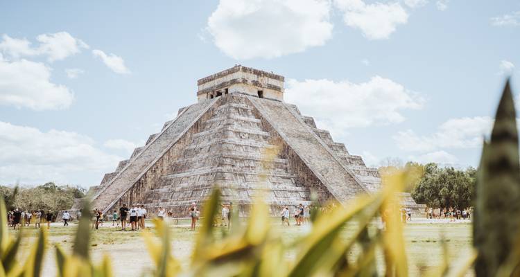 La majestuosa pirámide de El Castillo en Chichén Itzá se alza contra un cielo brillante mientras los visitantes exploran la base.