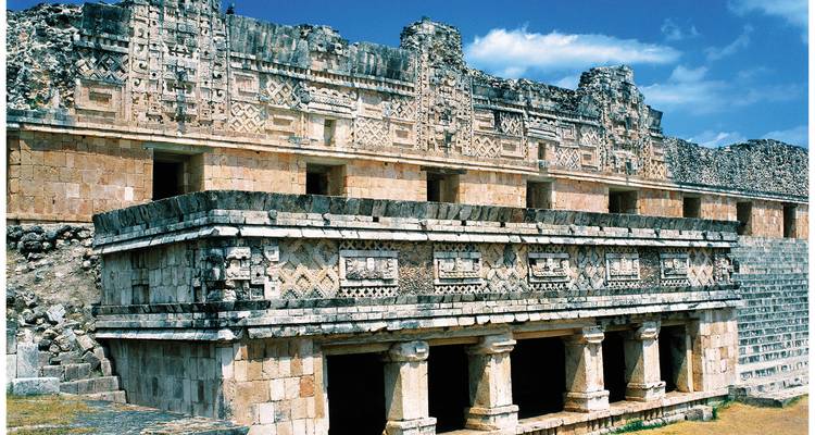 Fachada de piedra tallada y columnas del Cuadrángulo de las Monjas en Uxmal bajo un cielo azul intenso.