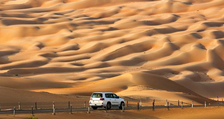 Weißer SUV fährt durch Sanddünen in einer Wüstenlandschaft.