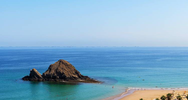 Malerischer Strand mit einer großen Felsformation im Meer.