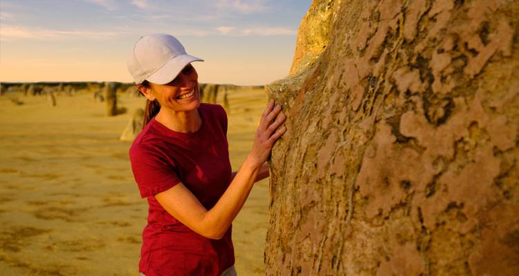Person lächelt neben einer Felsformation in einer Wüstenlandschaft.