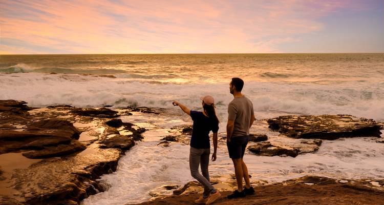 Zwei Menschen, die während eines lebendigen Sonnenuntergangs auf das Meer blicken.