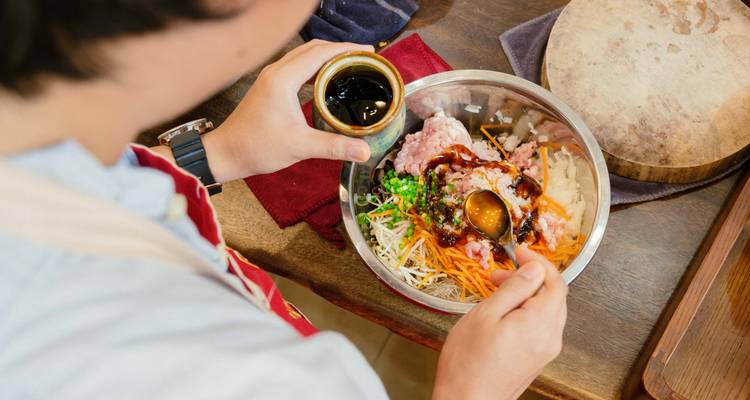Persoon die voorzichtig saus toevoegt aan een kom met ingrediënten.