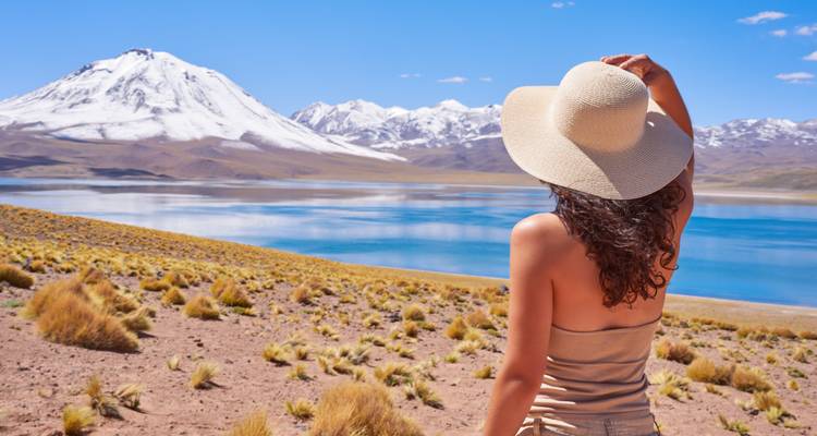 Frau mit Hut blickt auf einen See und schneebedeckte Berge.