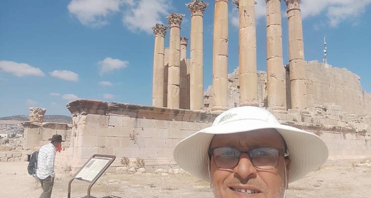 Homme avec un chapeau se tenant près de ruines anciennes avec de hautes colonnes.