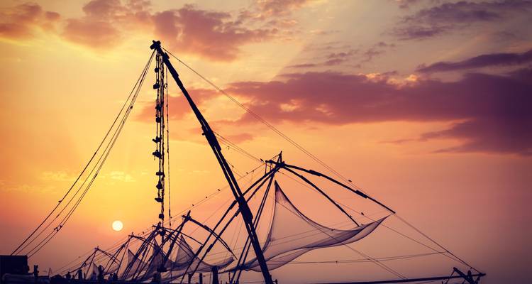 Redes de pesca chinas recortadas contra un cielo al atardecer de colores naranja y púrpura vívidos.
