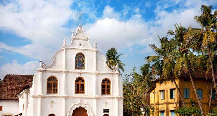 Iglesia colonial blanca enmarcada por palmeras bajo un cielo azul brillante.