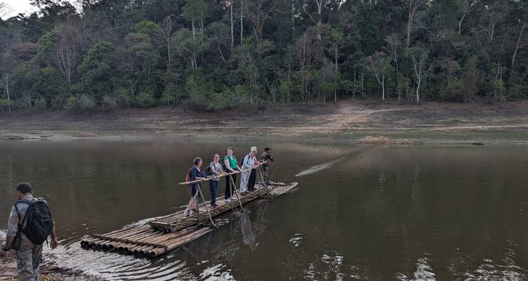 Los viajeros impulsan una simple balsa de bambú a través de un tranquilo lago en el bosque.