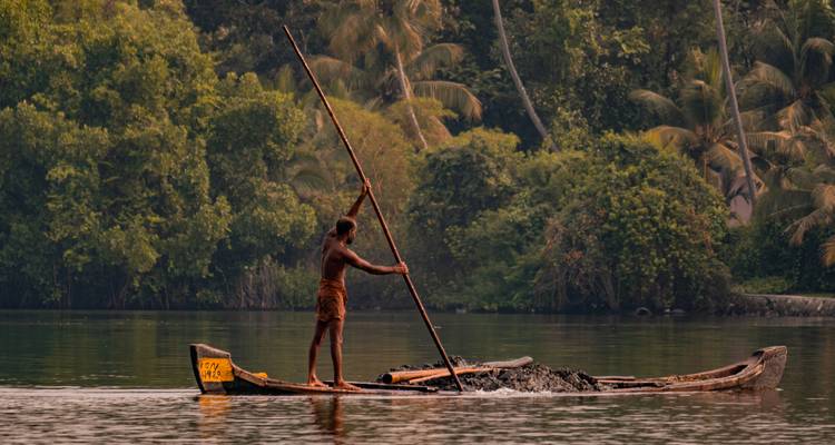 Un hombre local impulsa una canoa de madera a través de un paisaje de aguas tranquilas exuberantes con una pértiga larga.