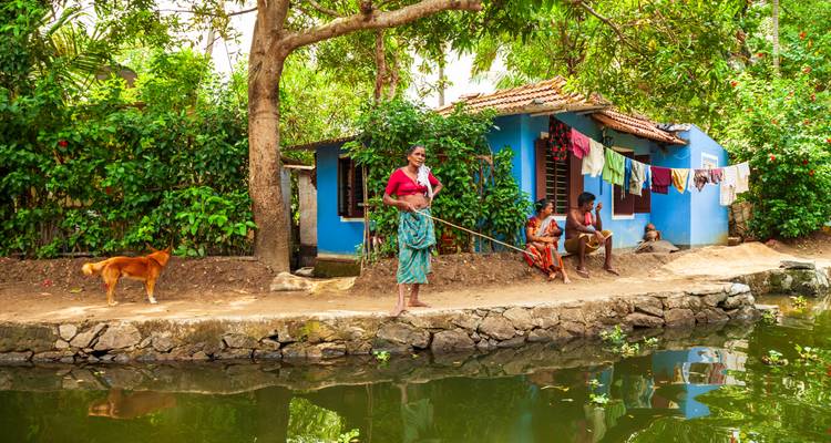 Una familia local y un perro descansando fuera de una casa azul a orillas del agua en los backwaters de Kerala.