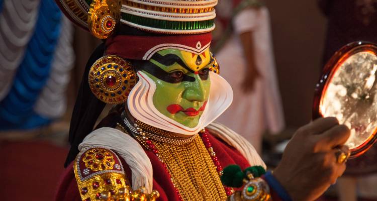 Primer plano de un intérprete de Kathakali con maquillaje verde vivido y un tocado elaborado.