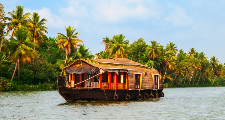 Una tradicional casa flotante de madera flota tranquilamente en una vía fluvial de Kerala rodeada de palmeras.