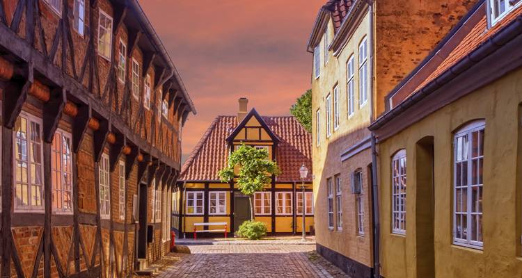 Charmante rue pavée bordée de maisons à colombages et aux couleurs pastel sous un ciel de coucher de soleil chaleureux.