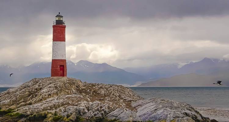 Le phare rouge et blanc des Eclaireurs perché sur un affleurement rocheux avec des montagnes brumeuses au-delà du canal Beagle.