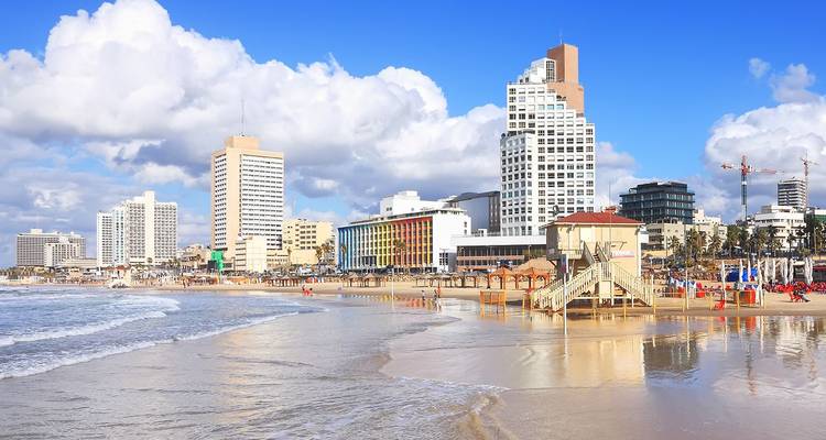 De moderne skyline van Tel Aviv verheft zich achter een zandstrand aan de Middellandse Zee onder wollige wolken.