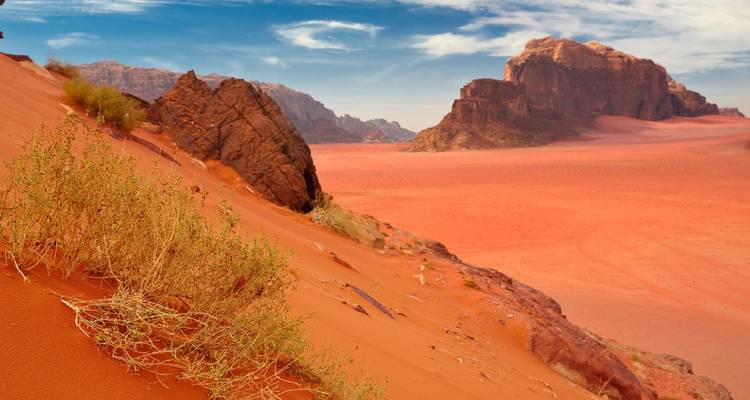 Red sands and dramatic rock formations of Wadi Rum under blue skies.