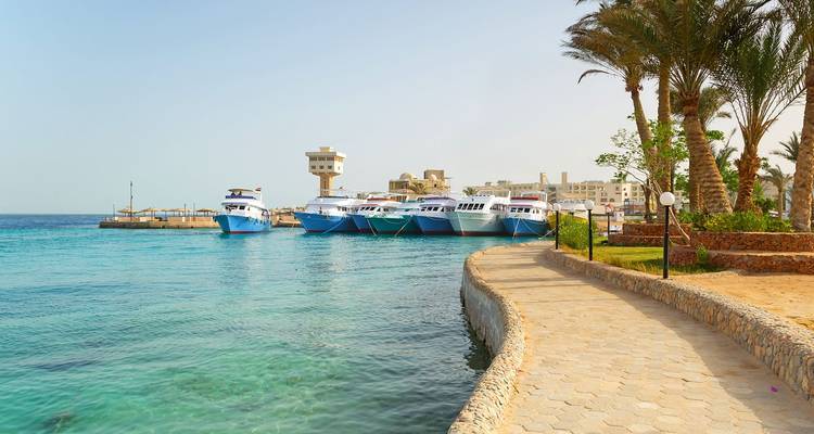 Calm turquoise harbor with moored yachts and palm-lined walkway in Hurghada.