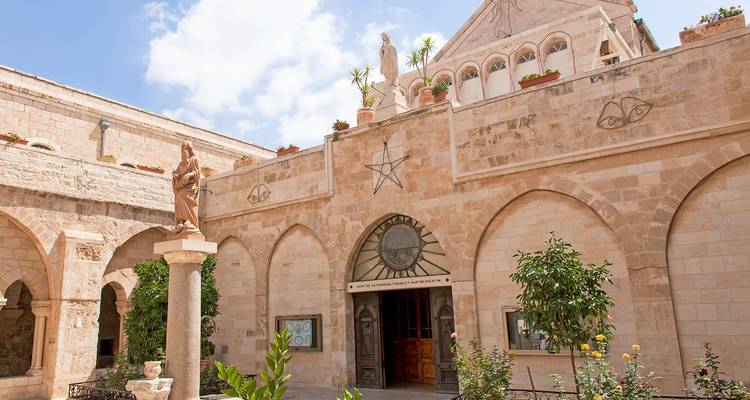 Stone courtyard of a historic church adorned with statues, plants and a star emblem.