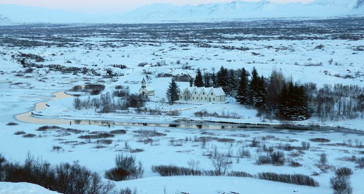 Llanuras cubiertas de nieve y un pequeño grupo de iglesias en el paisaje invernal del Parque Nacional Thingvellir con la luz del amanecer en tonos pastel.