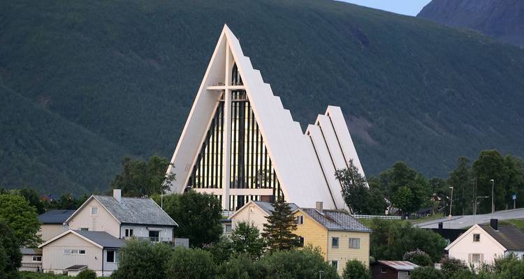 Catedral Ártica distintiva que se alza sobre casas con un telón de fondo de montaña boscosa.