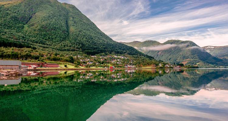 Fjord miroir reflétant des collines vertes, des maisons de village et des nuages effilés dans le ciel