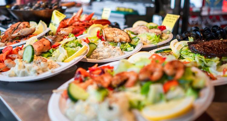 Close-up van uitgestalde zeevruchten en salades op borden bij een levendige marktkraam.