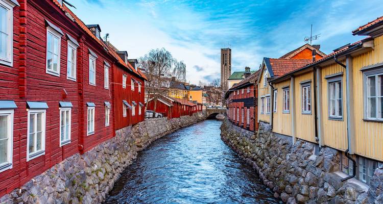 Casas de madera de colores vivos flanquean un estrecho canal que fluye a través de un pueblo sueco histórico.