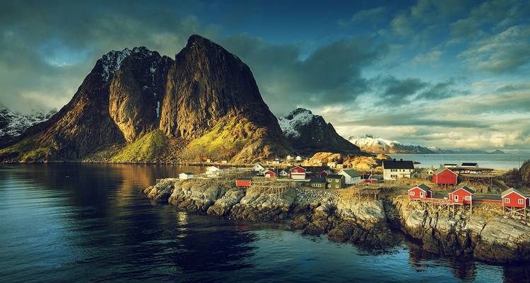 Las cabañas rojas de los pescadores se aferran a las costas rocosas bajo los picos imponentes al atardecer en las Islas Lofoten.