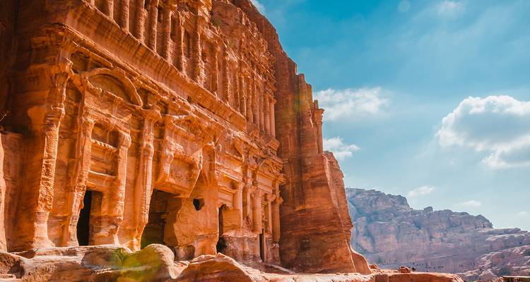Ancient rock-cut architecture with blue sky and mountain backdrop.